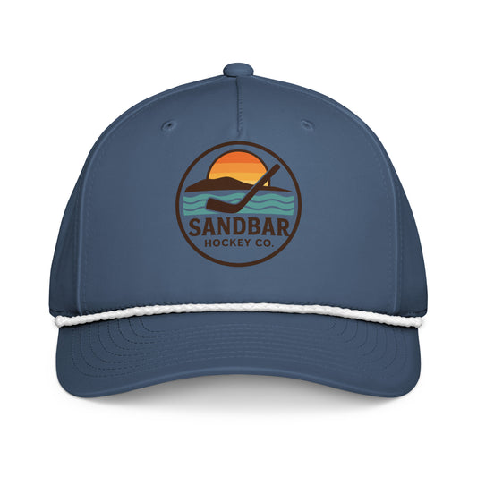 Blue hockey rope hat front view with Sandbar Hockey Co. sunset puck logo and white rope detail.