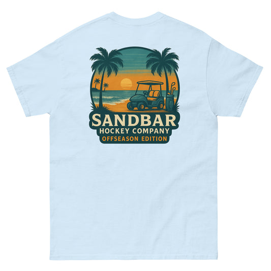 Light blue T-shirt with a large back graphic of a beach sunset scene featuring palm trees, ocean waves, a golf cart, hockey sticks, and the text “Sandbar Hockey Company Offseason Edition.”
