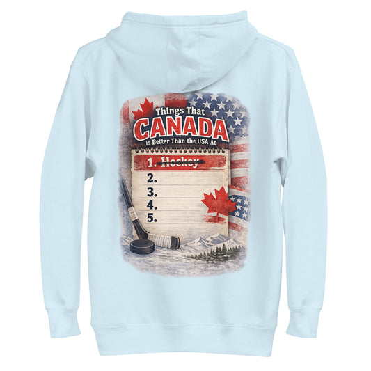 Light blue hockey hoodie with a large back graphic that says “Things That Canada Is Better Than the USA At,” featuring a notepad list with “1. Hockey” crossed out, plus Canadian and American flags, a hockey stick, puck, maple leaf, and mountain background.