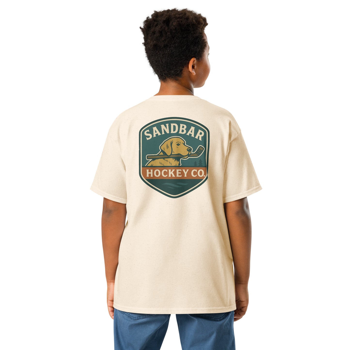 Youth natural Sandbar Hockey Dog Badge T-Shirt back view on model with large badge graphic of a dog holding a hockey stick in its mouth