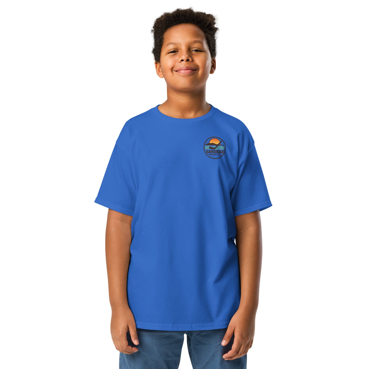 Blue youth hockey t-shirt front side on model with small circular Sandbar Hockey Co. sunset, water, island, and hockey stick chest logo
